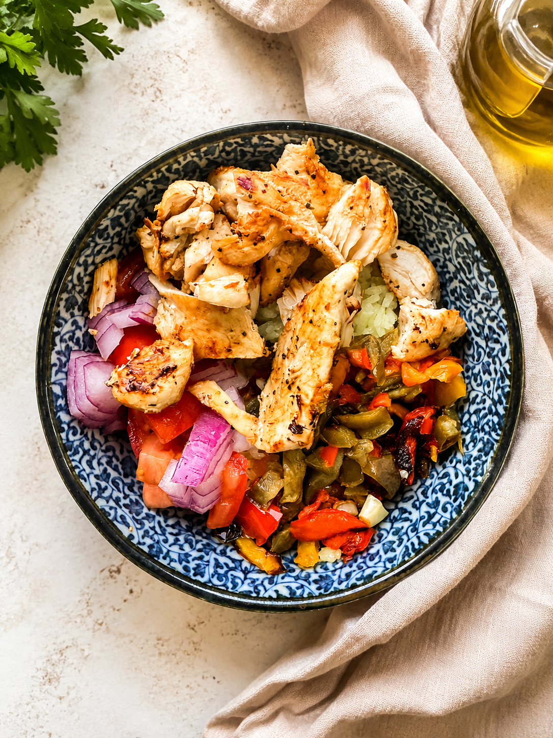 Grilled chicken Mediterranean bowl with rice, roasted peppers, tomatoes, red onion, and fresh vegetables in a blue ceramic bowl.